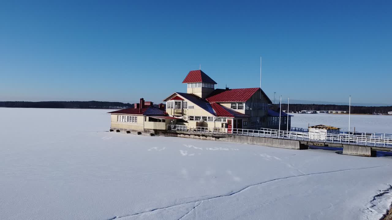 얼어붙은 호수에 둘러싸인 상징적인 레스토랑, 핀란드의 은 날, 은 파란 하늘 아래 눈으로 인 표면, 거대한 눈 인 풍경이 지평선에 걸쳐 펼쳐져, 평온한 겨울 풍경을 보여줍니다.