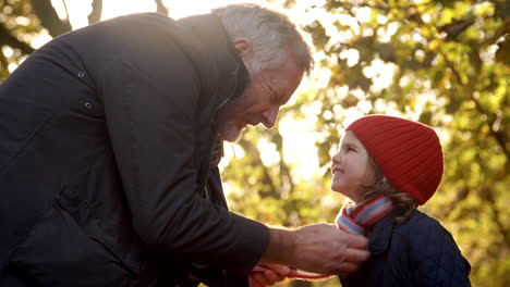 abuelo atando la bufanda de la nieta en una caminata de otoño