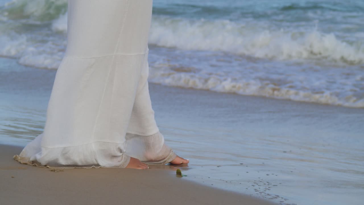 pies de una mujer joven jugando en la arena dorada de una isla tropical con olas en el fondo