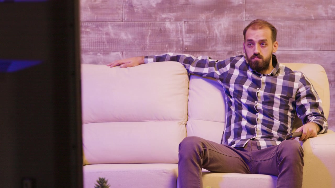Uomo barbuto che guarda la televisione su un divano a casa
