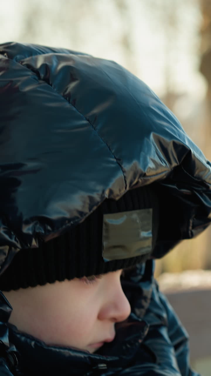 벤치에 가까이 앉아있는 아버지와 아들의 클로즈업, 둘 다 집중적으로 보이며, 아들은 검은색 재을 입고, 아버지는 갈색 재를 입고, 자연의 흐릿한 배경을 가지고 있습니다.