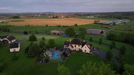 Luxury american mansion with Swimming pool in rural suburb located on hillside. Aerial orbit wide shot. Sunset time at dusk with yellow farm fields in distance. Aerial wide shot. Pennsylvania, USA.