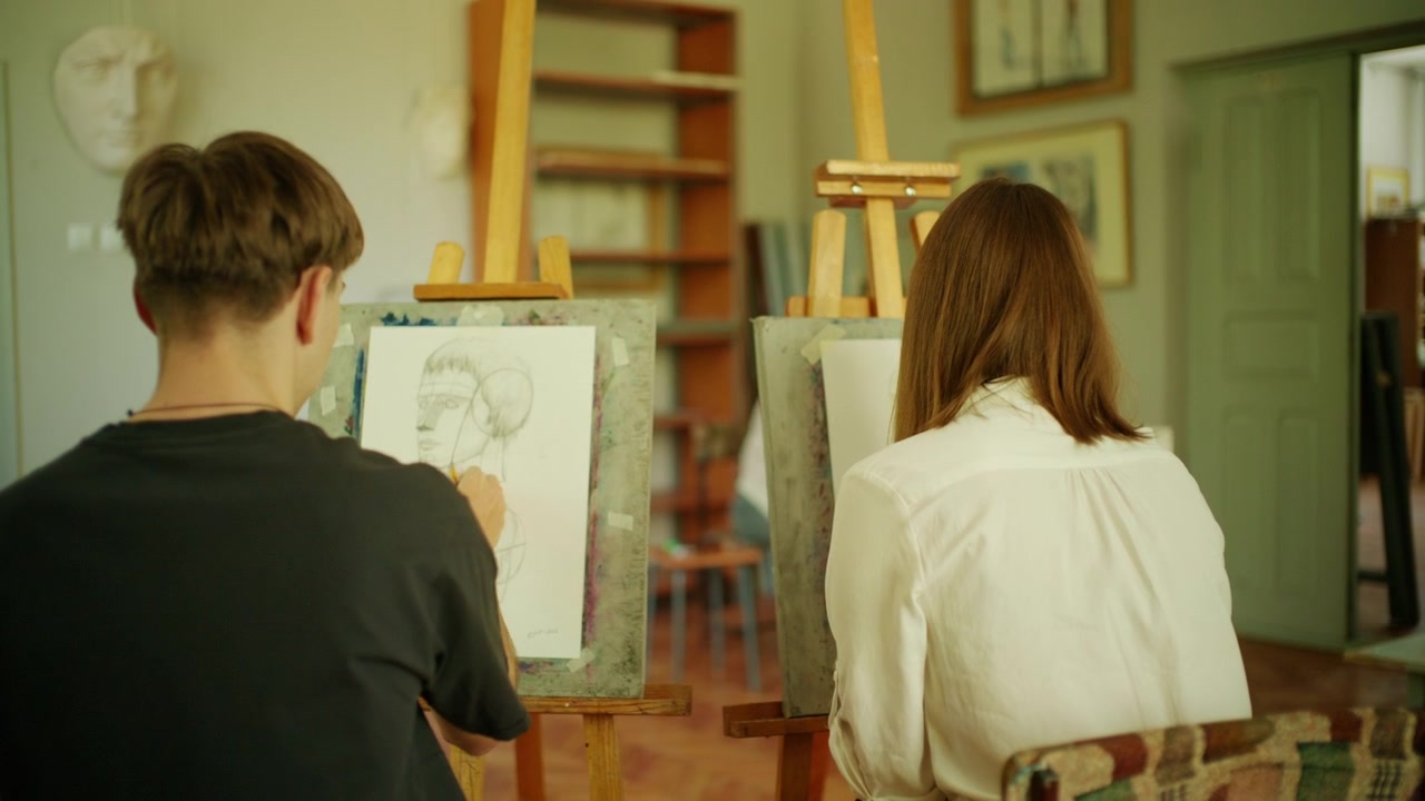 Bir sanat stüdyosu sınıfında şövalelerde eskiz yapmaya odaklanmış öğrencilerin arkadan görünümü.