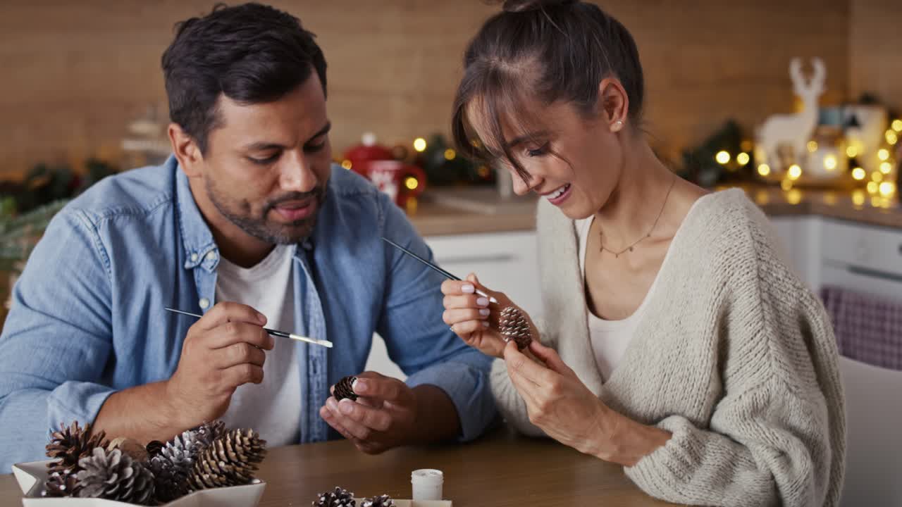 una pareja multiétnica decorando el cono con pintura blanca durante la época navideña en casa.
