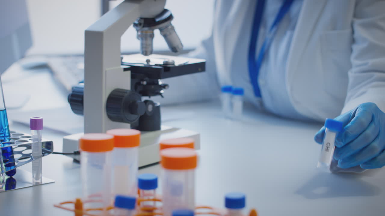 primer plano de un trabajador de laboratorio que realiza investigaciones utilizando un microscopio que sostiene un tubo de ensayo etiquetado chi