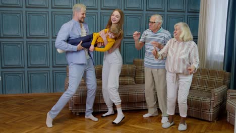 family members of different generations having fun listening music, dancing crazy in room at home