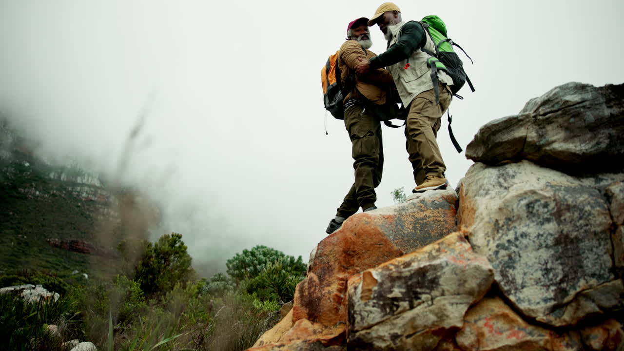Hikers helping each other climb a mountain