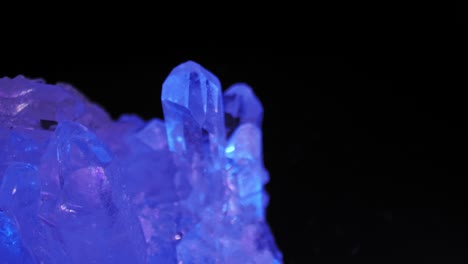 Quartz-clear-crystal-glimmering-in-purple-light-against-black-background