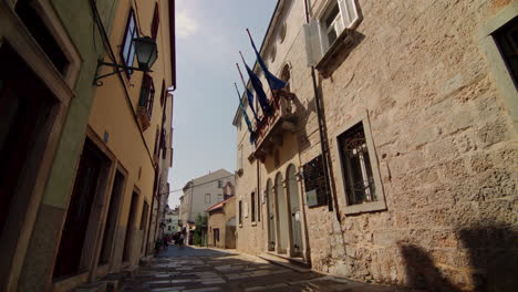 blue flags wave in wind from balcony of historic stone building in cres, croatia