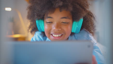 niño en el dormitorio acostado en la cama usando auriculares usando tableta digital