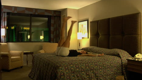 una mujer joven salta hacia atrás sobre la cama de una habitación de hotel