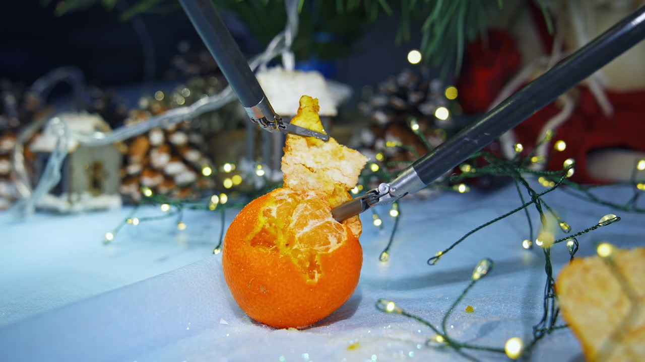 High-tech equipment peeling mandarin. Metal cybernetic tools on Christmas decorations background. Futuristic innovations.
