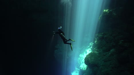 a diver swims out of a beam of light into darkness off the coast of mexico's yucatan peninsula