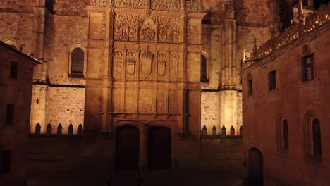 aerial view coming closer to historical neoclassical facade filled with engravings illuminated at night in salamanca, spain