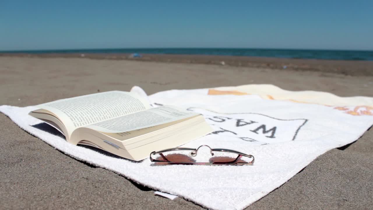 ⁇ 은 해변에 누워 있는 수건 위에 열린 책 바람이 페이지를 뒤집고 있다 1