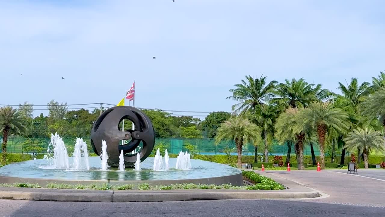 A circular sculpture with a fountain surrounded by lush palm trees under a clear sky.