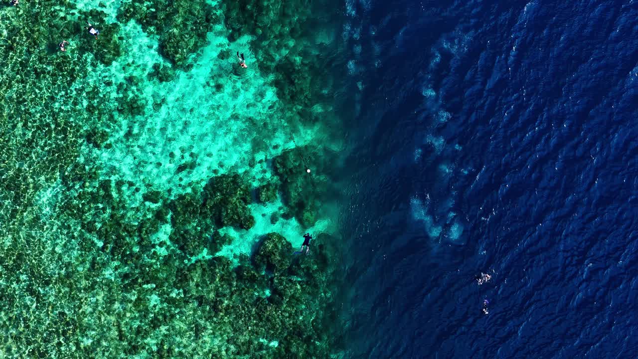 Pessoas praticando snorkel no recife de Moalboal e no oceano azul profundo, vista aérea de cima para baixo