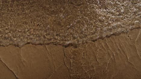 a gentle wave rolls onto rippled sand, capturing textures and light reflections along the algarve shoreline in portugal