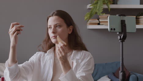 Young-Cute-Vlogger-Woman-Reviewing-A-Wooden-Gua-Sha-And-Using-It-On-Her-Face-While-Recording