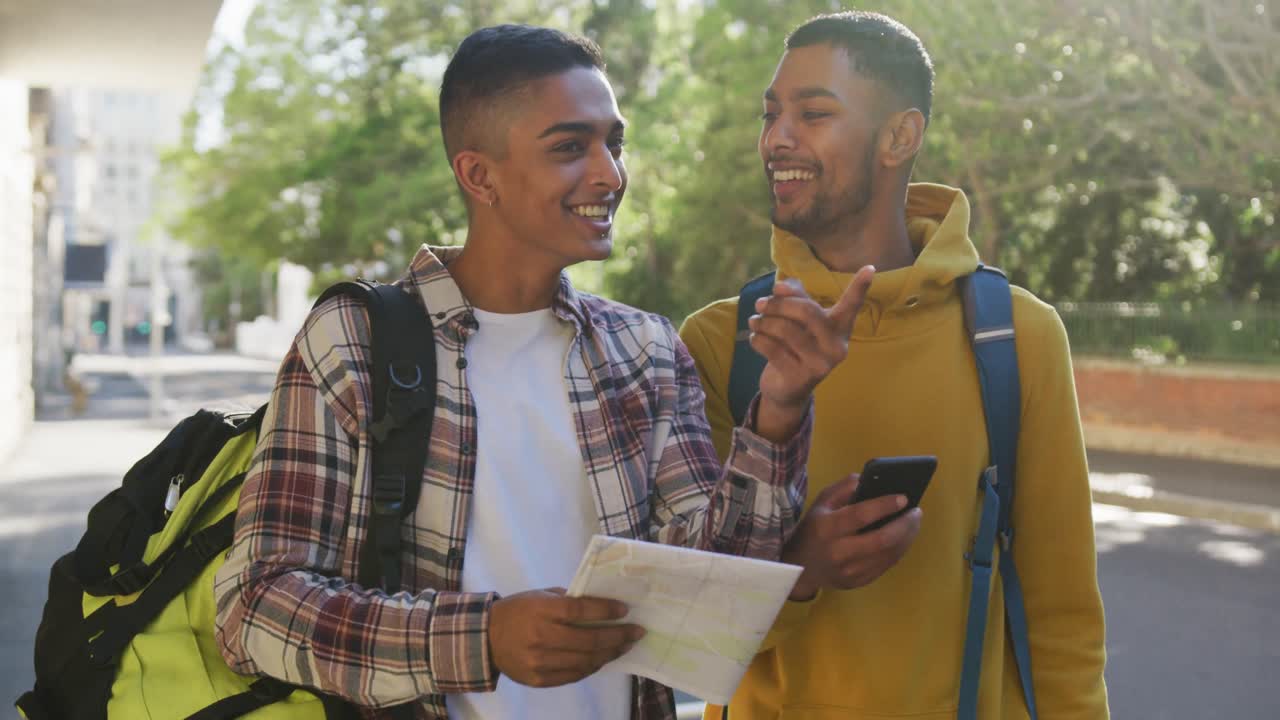 dos felices amigos de raza mixta usando un teléfono inteligente y un mapa en la calle