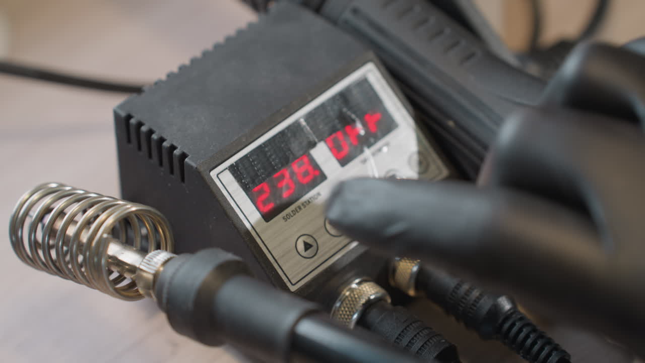 손바닥에 장갑을 입은 손이 솔더링 스테이션에서 디지털 온도 조절을 조정하여 온도를 242도에서 238도로 변경합니다.
