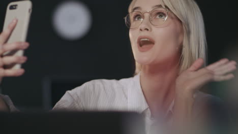 Cheerful-woman-sending-air-kiss-for-mobile-selfie-in-night-office