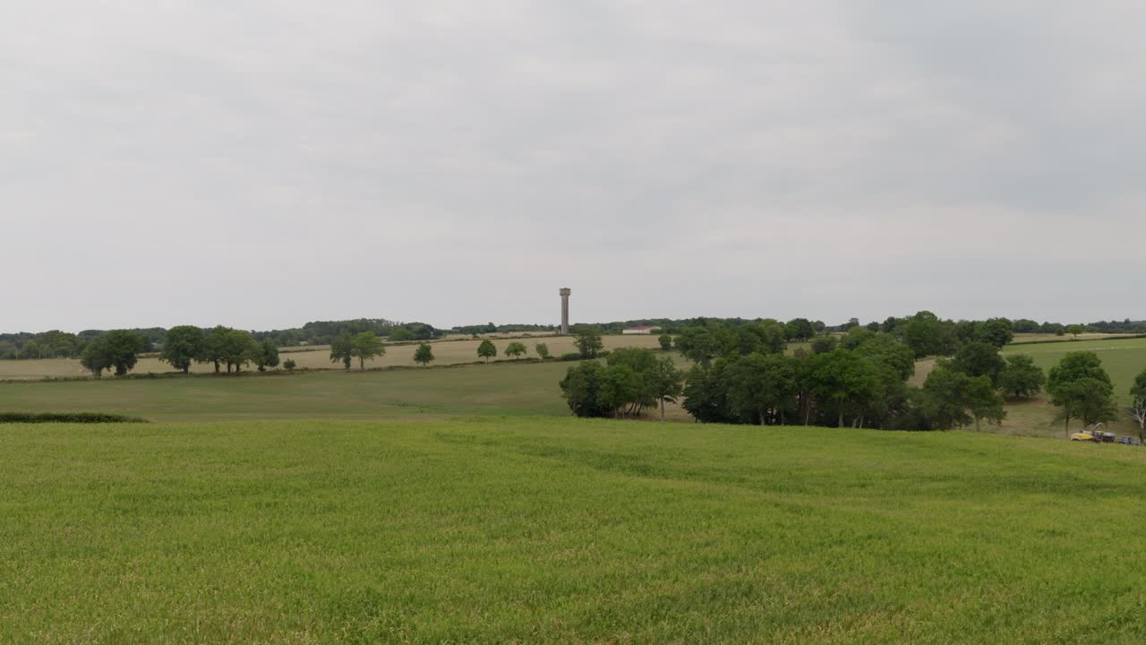 Aerial drone view of wide green fields, farmland, and scattered trees stretching into the countryside beneath an overcast sky