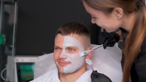 a young man receives a nourishing facial mask from a beautician in a spa salon, close-up. spa treatments and skin care. vertical video.
