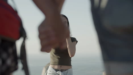 smiling girl standing on cliff edge, holding camera and taking photo of two people