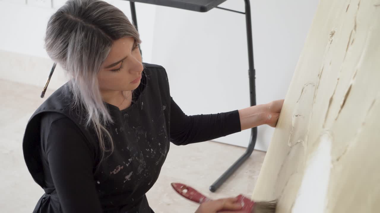hábil artista latina sentada en el suelo haciendo un enorme lienzo abstracto
