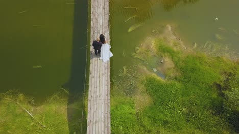 newlywed-couple-walks-along-old-bridge-over-river-aerial