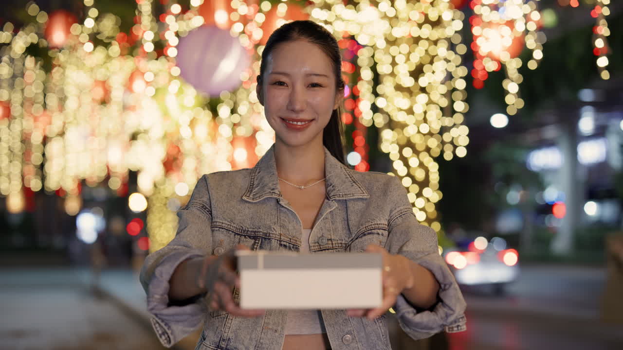 Woman holding a gift in front of street lights