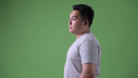 young handsome overweight asian man against green background