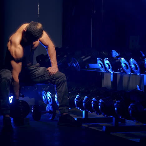 muscular man working out in gym doing exercises with dumbbells, strong male naked torso, abs. blue light filter in sport gym. selective focus.
