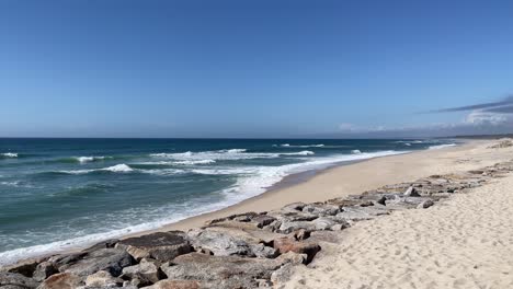 Olas-Lavando-En-Una-Larga-Playa-De-Arena-Con-Rocas,-Furadouro,-Portugal