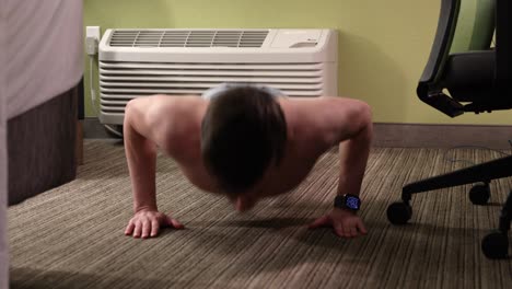 hombre joven, blanco, sin camisa, haciendo 50 flexiones en su habitación de hotel junto a la unidad de aire acondicionado en jeans