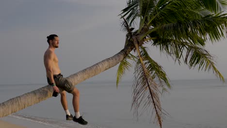 middle aged male enjoying sunset while sitting on hanging palm tree above the tropical beach in thailand.