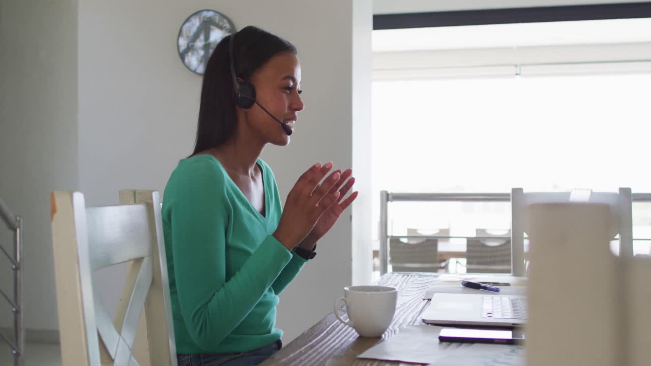 African american woman wearing phone headset talking on video chat on laptop while working from home