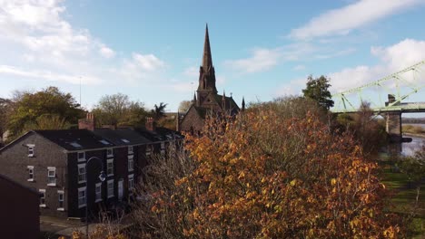 rising over autumn trees to reveal small town church with steeple alongside runcorn bridge