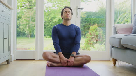 portrait of smiling mature man sitting on mat at home in yoga position meditating