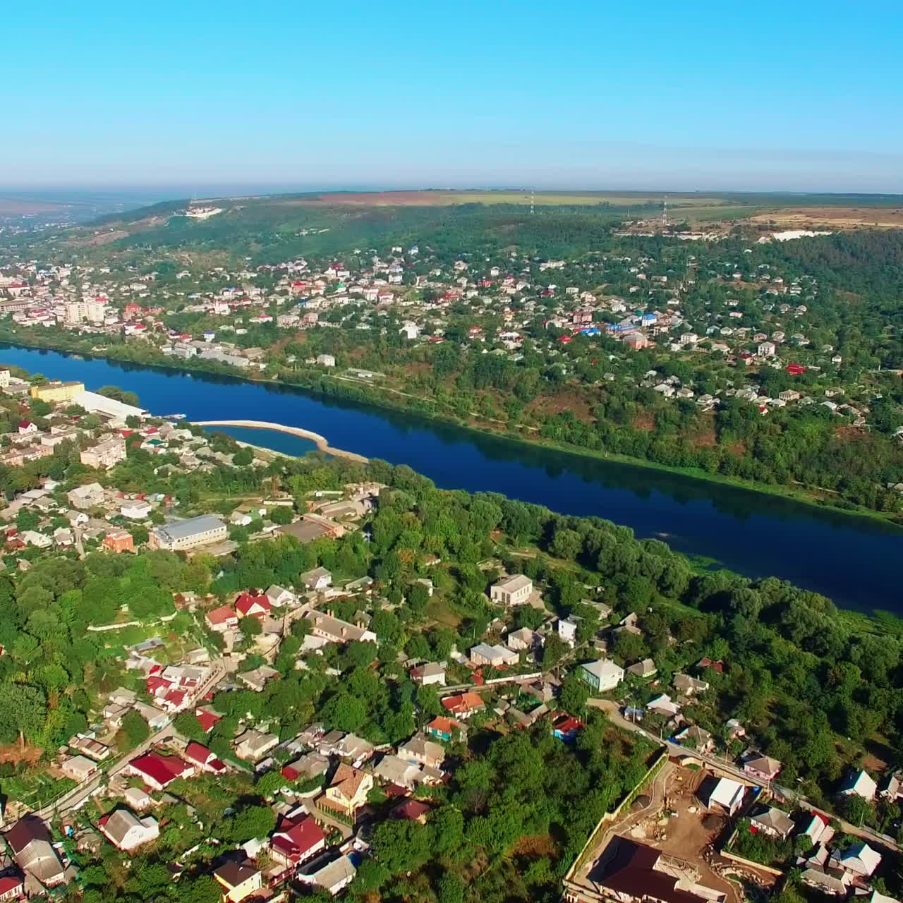 Dark blue river dividing the city into two parts. Dense architecture mixed with the beautiful greenery at backdrop of blue clear sky. Top view