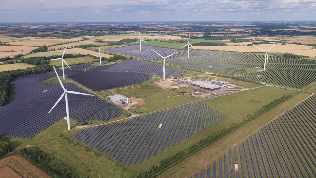 Sunny aerial view of wind turbines and solar panels on a lush English farm under a clear blue sky.
