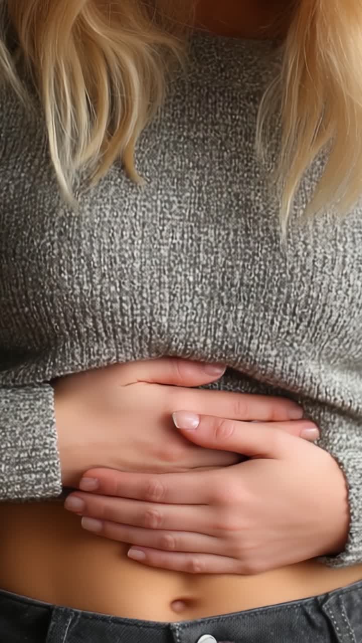 Un momento contemplativo: una persona si tiene delicatamente lo stomaco, riflettendo su possibili preoccupazioni o disagi, mentre indossa un maglione grigio lavorato a maglia, che evoca calore e introspezione