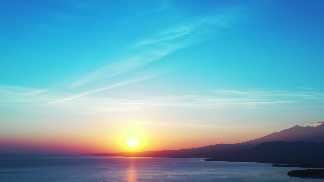 Paradise heaven with yellow sun setting down ocean and mountains horizon, rainbow colors on glowing sky at sunset in Indonesia