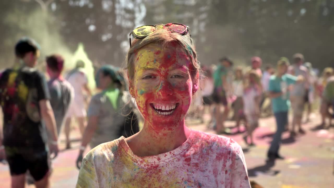 Young happy girl in colourful powder is smiling on holi festival in daytime in summer, watching at camera, color concept, emotional concept