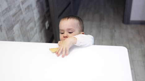 beautiful kid comes up to the table. baby reaching his hand to pick up a cookie from table. child takes a treat and leaves. top view.