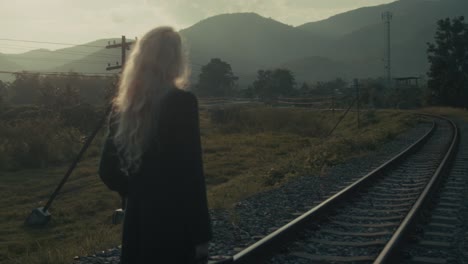 woman walking along train tracks at sunset