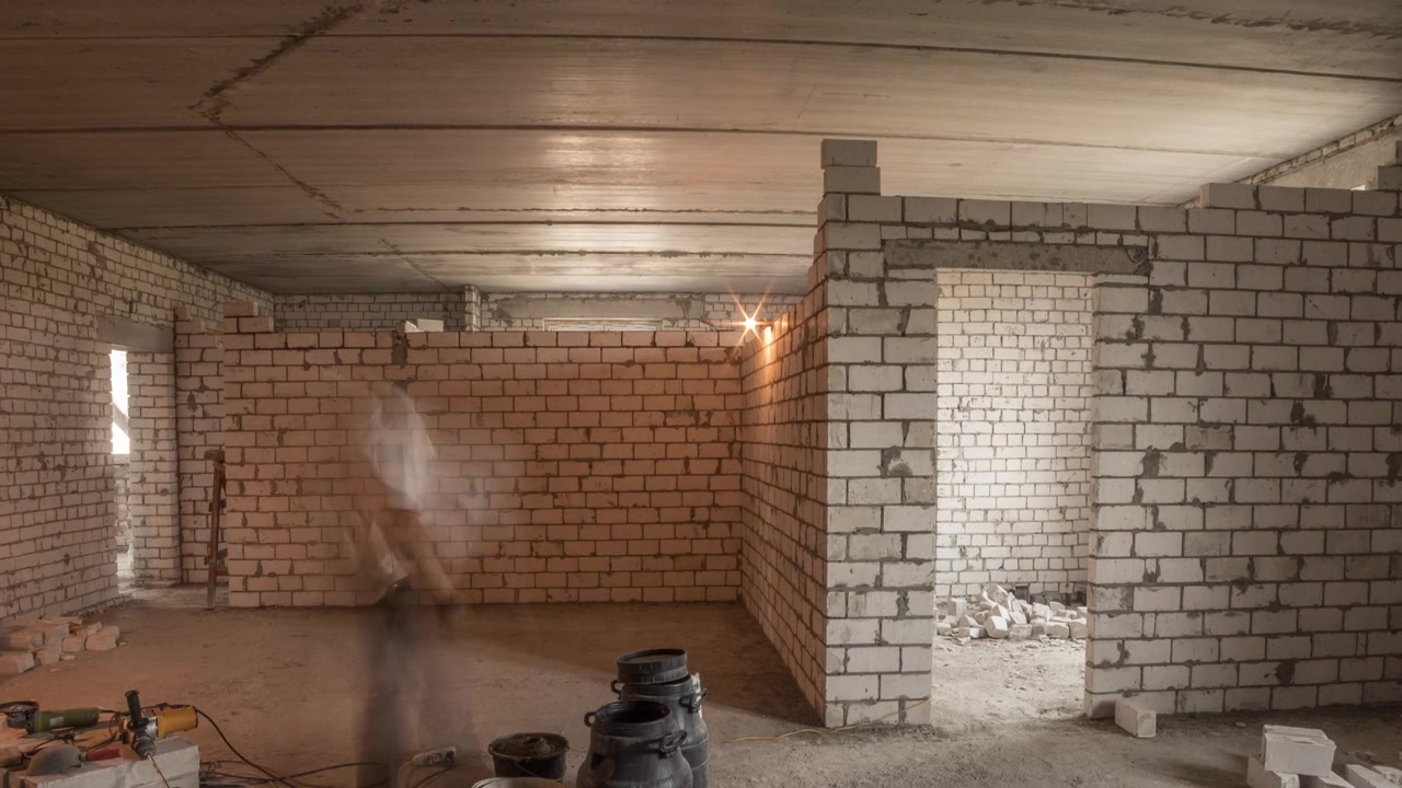 Muratori che posano pareti in mattoni all'interno di un appartamento con attrezzi professionali in timelapse. Operai al lavoro, muratori che costruiscono un muro, appaltatore e operaio. Materiali da costruzione intorno.