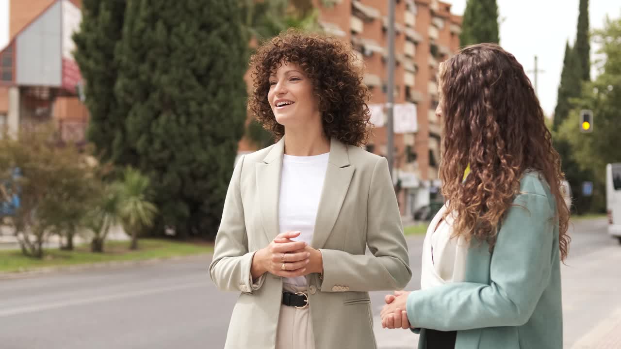 Happy businesswomen conversing while signaling taxi near street