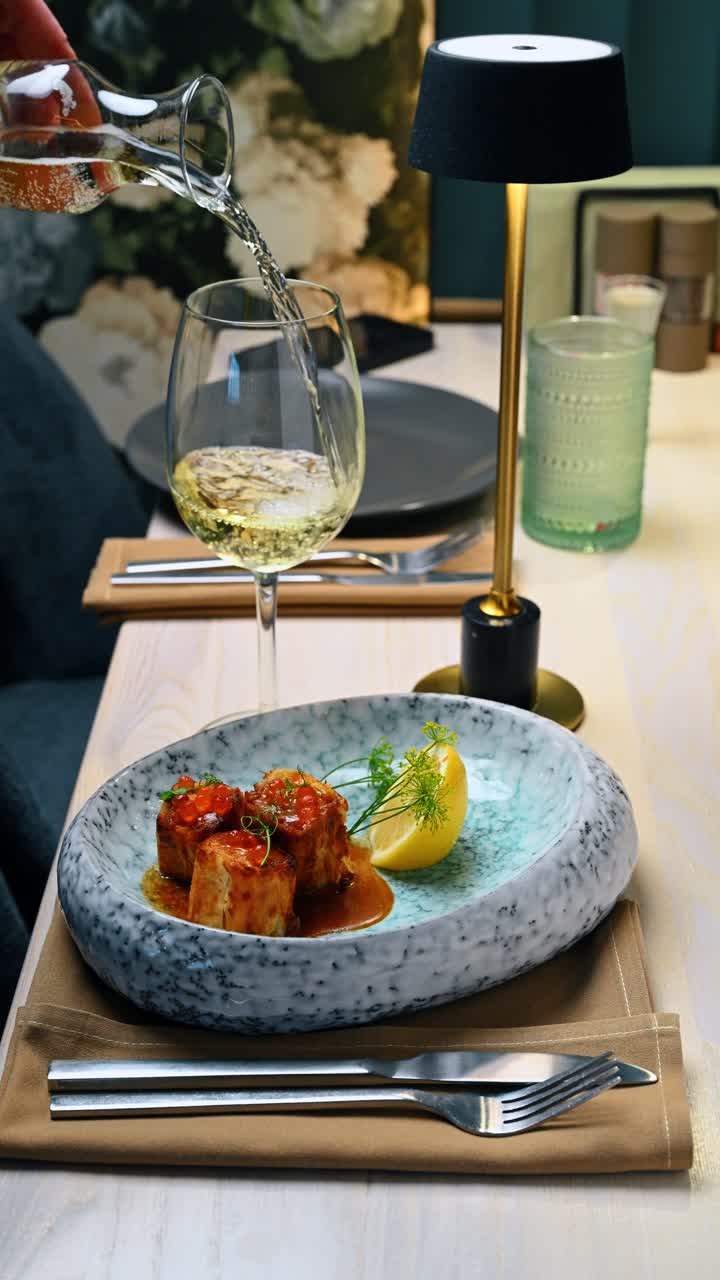 Vino bianco versato nel bicchiere accanto a un piatto di pesce. Una mano versa vino bianco da una caraffa in un bicchiere su un tavolo con un antipasto di pesce gourmet.